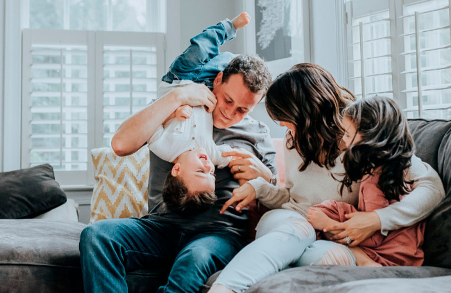 familia en una sala con una actitud muy alegre, la familia cuenta con cuatro integrantes padre, madre, hijo y hija.