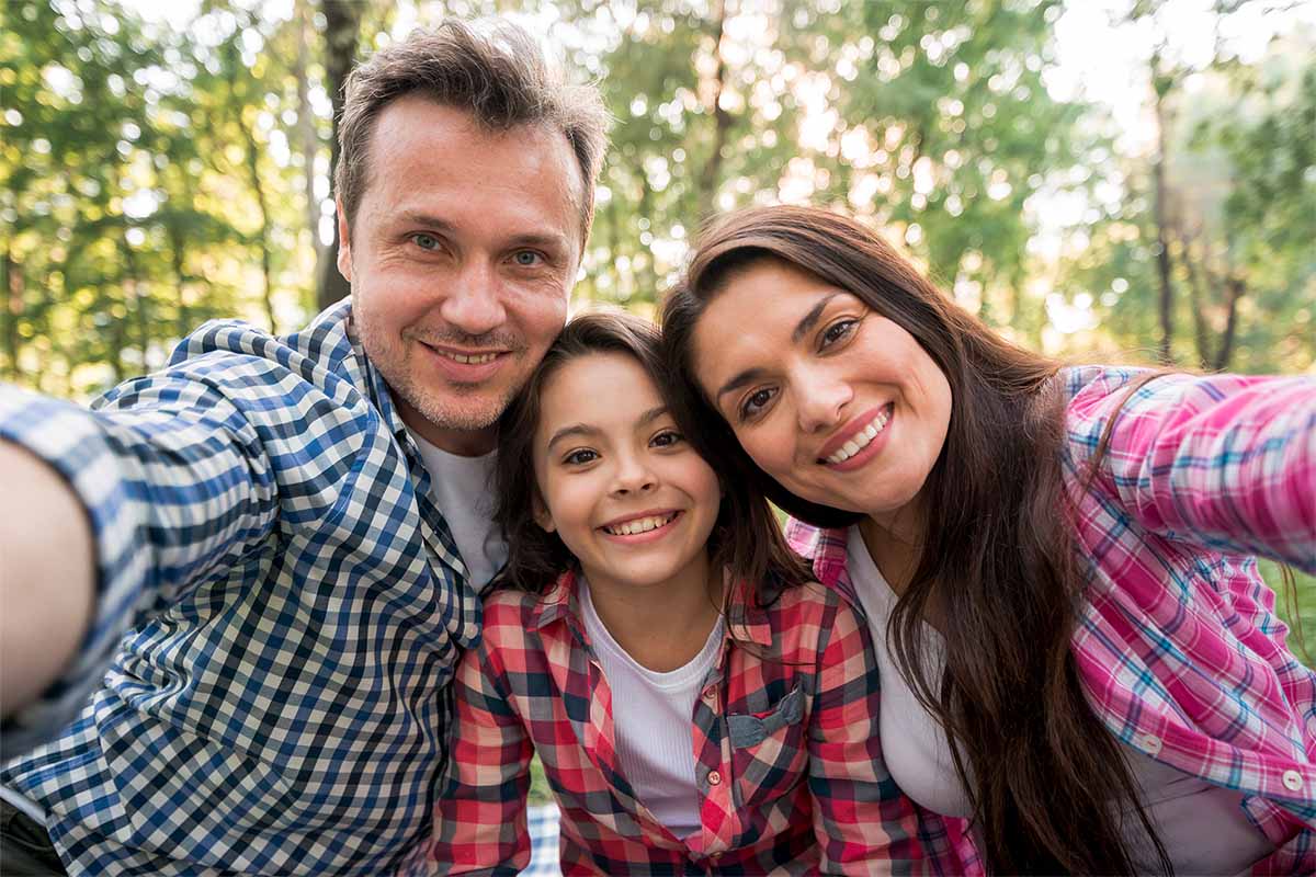 Familia tomando una foto tipo selfie en un parque, la cual está formada por 3 integrantes: mamá, papá e hija.