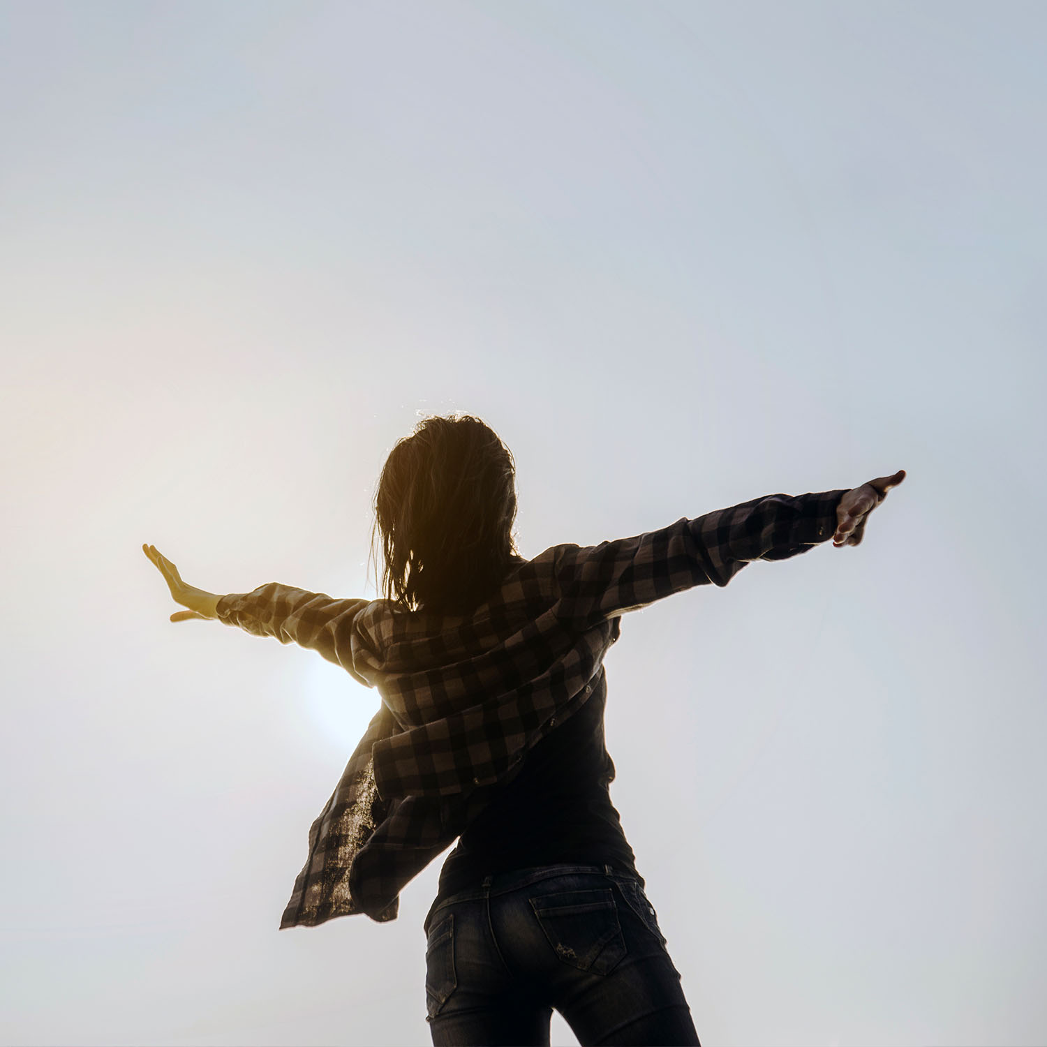 Mujer de espalda abriendo los brazo y mirando al cielo.