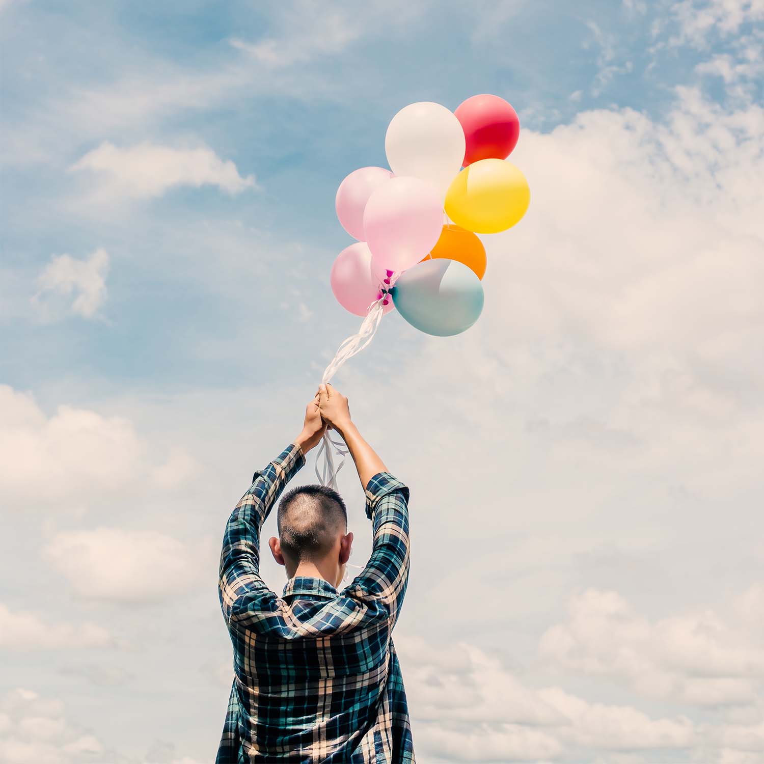 Niño levantando las manos hacia el cielo, sosteniendo un manojo de globos; estos están flotando.