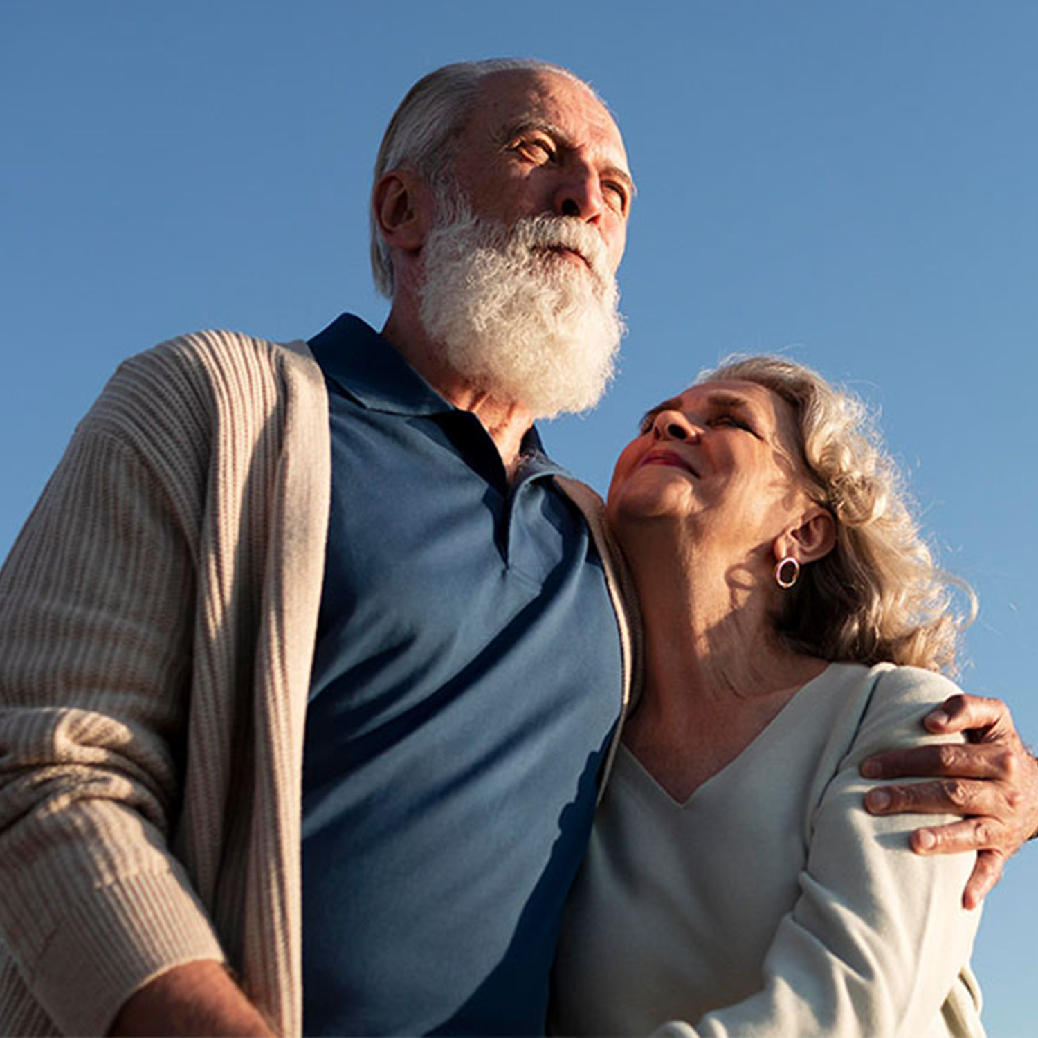 Pareja de adultos mayores abrazados, viendo hacia el cielo.