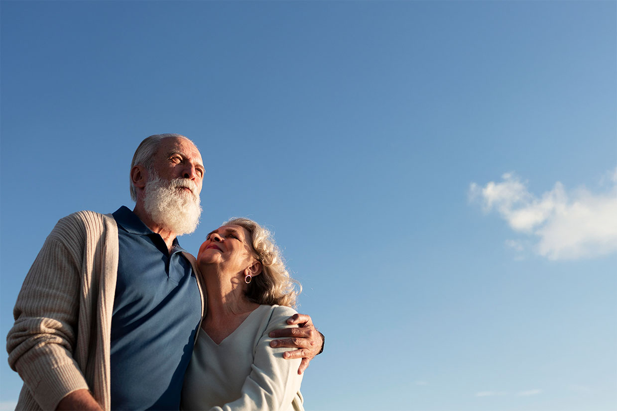 Pareja de adultos mayores abrazados, viendo hacia el cielo.