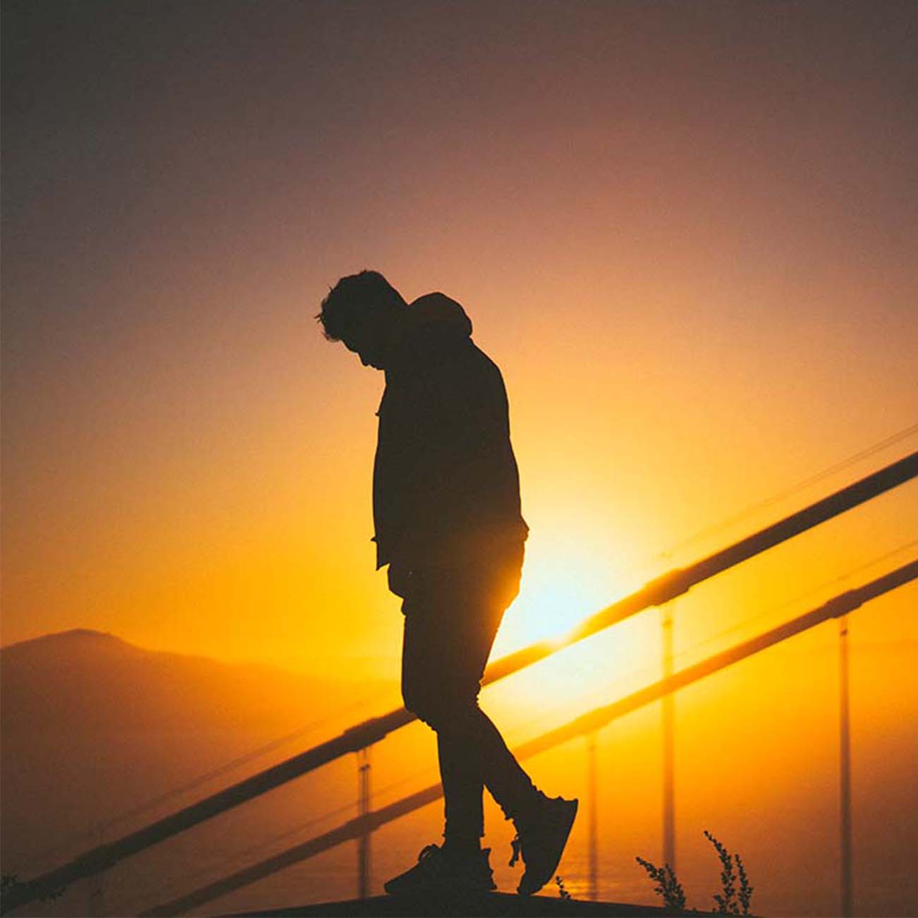 Perna bajando unas escaleras al fondo se ve el atardecer y el sol ocultándose.