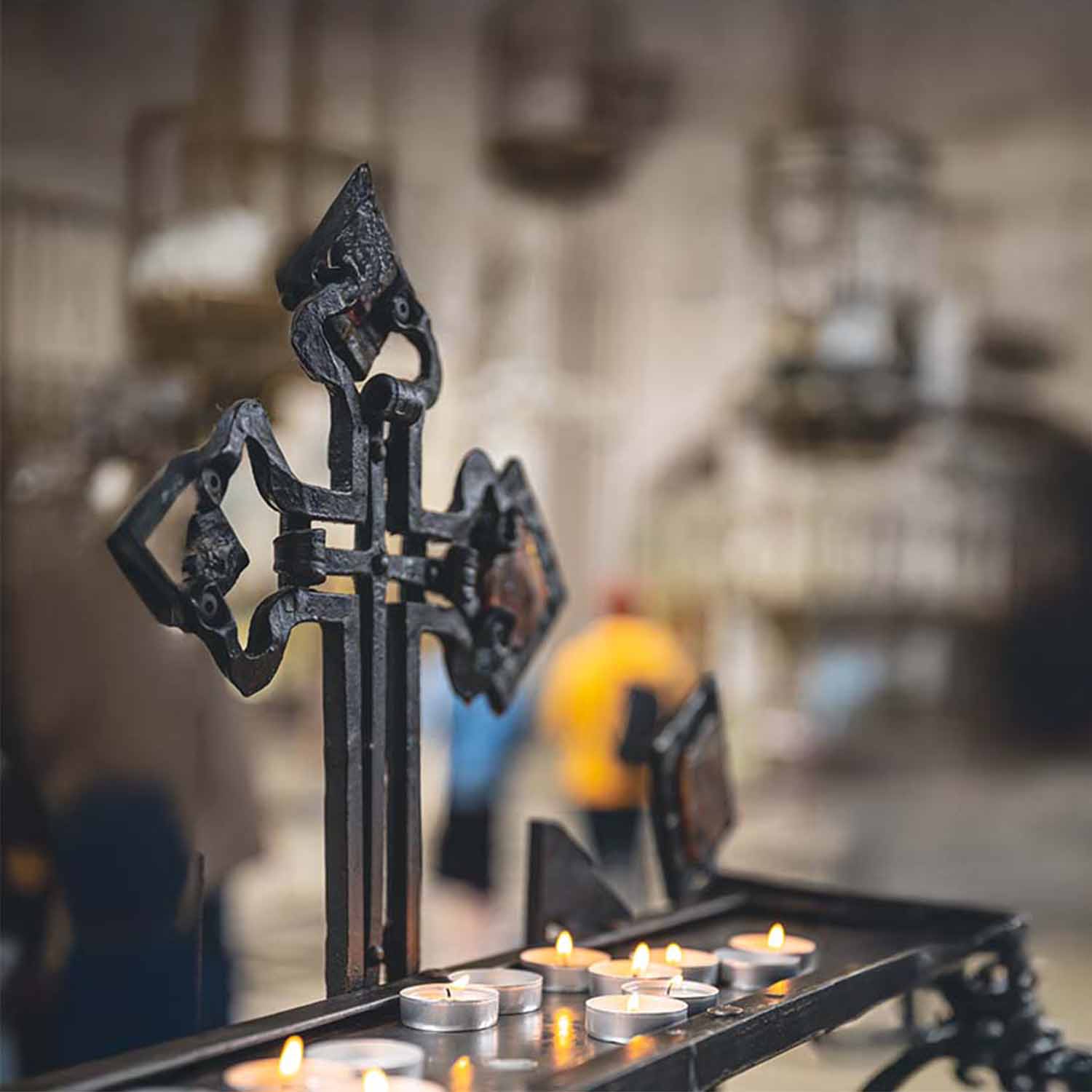 Altar con una cruz de hierro y velas debajo de ella, este altar esta situado dentro de una iglesia.
