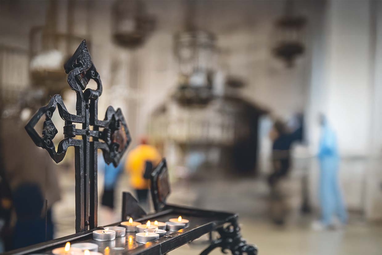 Altar con una cruz de hierro y velas debajo de ella, este altar esta situado dentro de una iglesia.