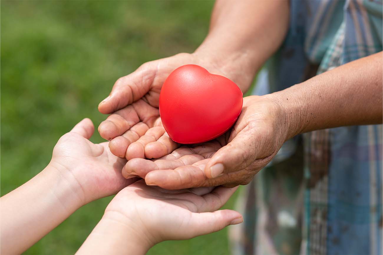 Persona de edad avanzada dándole un corazón de platico a una persona joven, como un símbolo de donación de órganos.