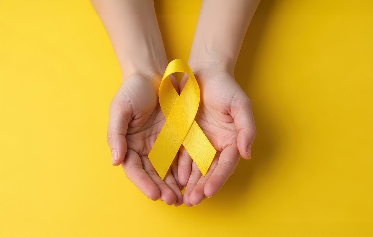Manos sostenido un listón entrelazado de color amarillo símbolo del mes para la prevención del suicidio.